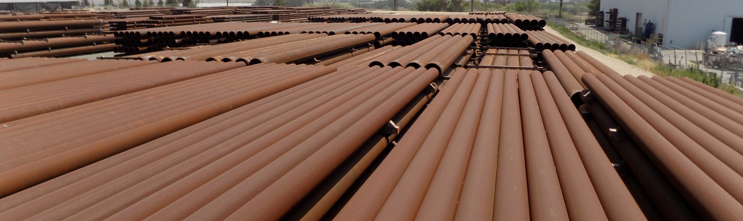 Team of rust-colored carbon steel piling pipes laid out in row.